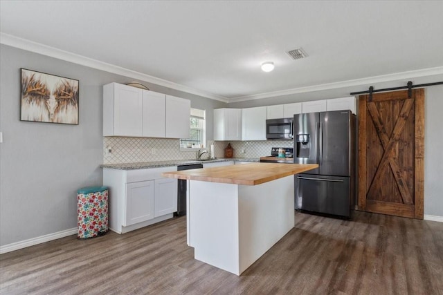 kitchen featuring butcher block countertops, white cabinets, a center island, stainless steel appliances, and a barn door