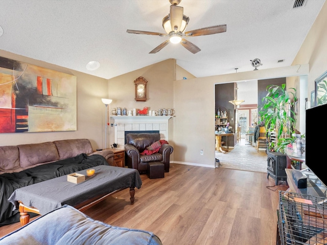 living room with ceiling fan, wood-type flooring, a textured ceiling, vaulted ceiling, and a fireplace