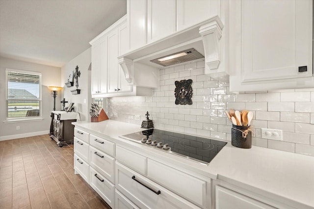 kitchen with dark wood-type flooring, black electric stovetop, tasteful backsplash, white cabinetry, and custom range hood