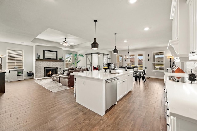 kitchen featuring stainless steel dishwasher, decorative light fixtures, a center island with sink, white cabinets, and light wood-type flooring