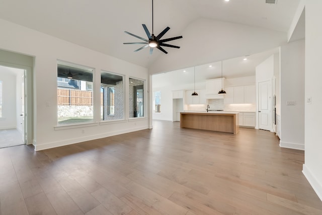 unfurnished living room with sink, high vaulted ceiling, ceiling fan, and light hardwood / wood-style floors