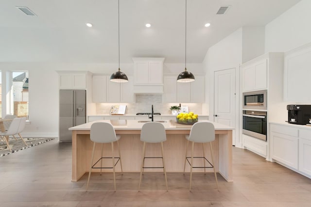 kitchen featuring an island with sink, appliances with stainless steel finishes, white cabinets, and pendant lighting