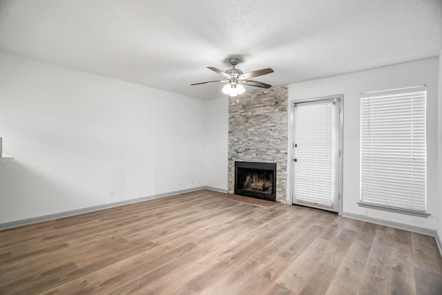 unfurnished living room with a stone fireplace, ceiling fan, light hardwood / wood-style floors, and a textured ceiling