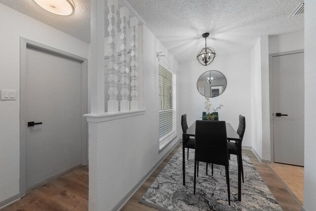 hall with light hardwood / wood-style flooring, a textured ceiling, and an inviting chandelier