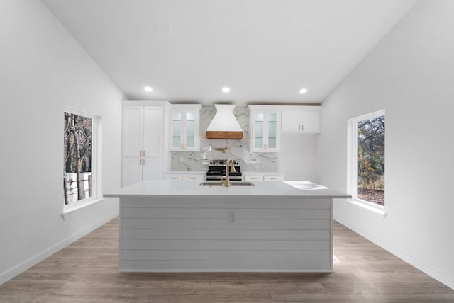 kitchen with white cabinetry, sink, backsplash, a center island with sink, and custom range hood