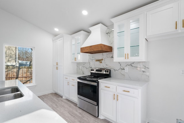 kitchen featuring backsplash, premium range hood, light hardwood / wood-style floors, white cabinetry, and stainless steel range with electric cooktop