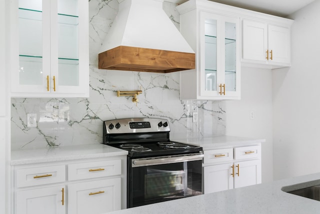 kitchen with light stone countertops, backsplash, premium range hood, electric stove, and white cabinets