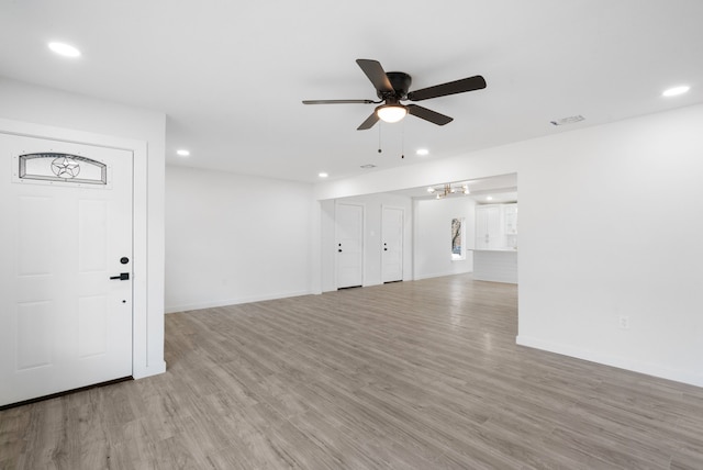 unfurnished living room with ceiling fan with notable chandelier and light wood-type flooring