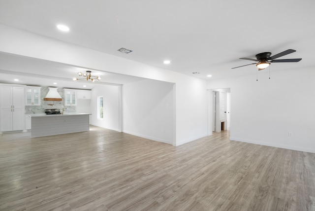 unfurnished living room featuring light hardwood / wood-style flooring and ceiling fan with notable chandelier