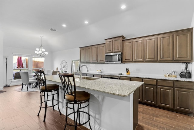 kitchen with light stone counters, sink, pendant lighting, a center island with sink, and a chandelier