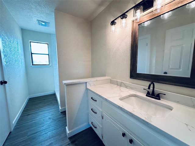 bathroom featuring baseboards, a textured wall, wood finished floors, a textured ceiling, and vanity