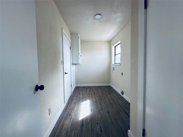 spare room featuring dark wood-style flooring, a textured wall, a textured ceiling, and baseboards