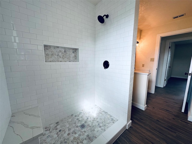 full bath with baseboards, visible vents, a tile shower, and wood finished floors