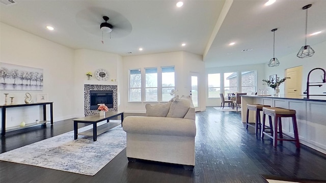 living room with sink, dark hardwood / wood-style floors, ceiling fan, and a tiled fireplace