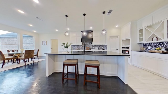 kitchen featuring tasteful backsplash, oven, white cabinetry, hanging light fixtures, and an island with sink