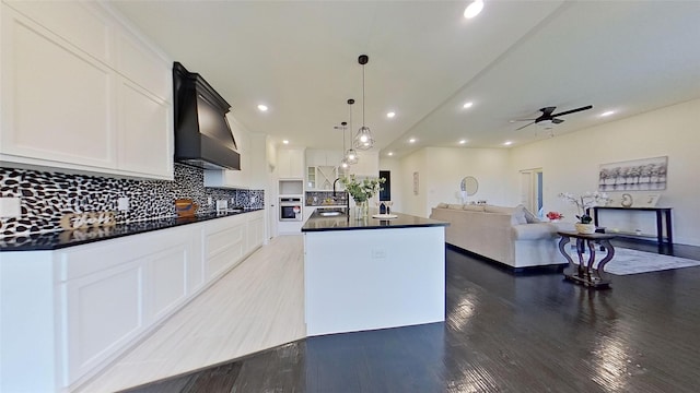 kitchen with premium range hood, a kitchen island with sink, pendant lighting, and white cabinets