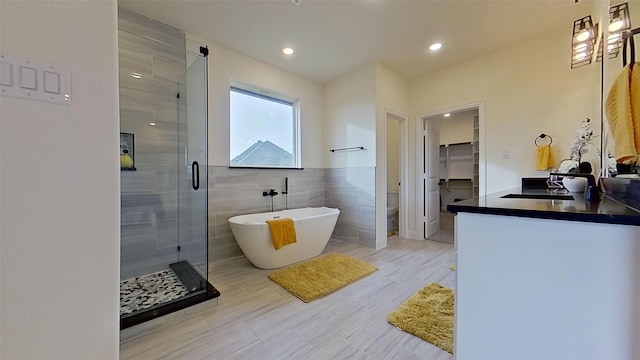 full bathroom featuring hardwood / wood-style floors, vanity, toilet, shower with separate bathtub, and tile walls