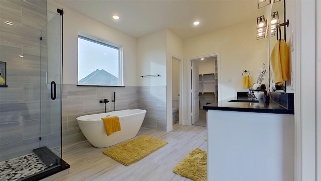 full bathroom featuring plus walk in shower, toilet, vanity, tile walls, and hardwood / wood-style flooring