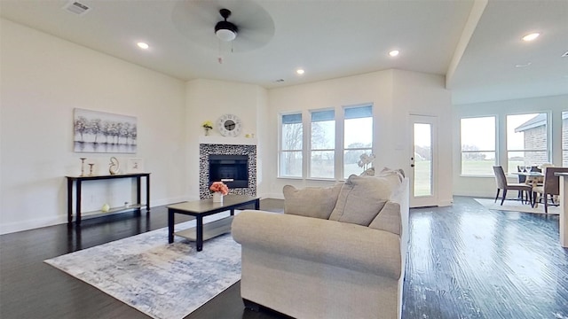 living room featuring dark wood-type flooring, ceiling fan, and a tiled fireplace