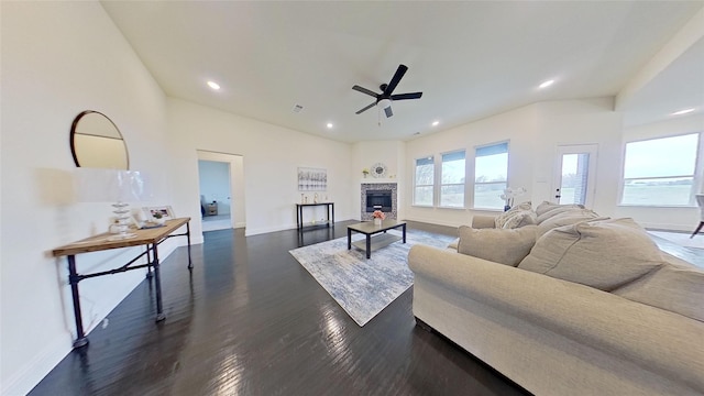 living room with a stone fireplace, dark wood-type flooring, and ceiling fan