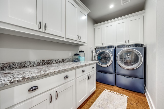 washroom featuring cabinets, washing machine and dryer, and light wood-type flooring