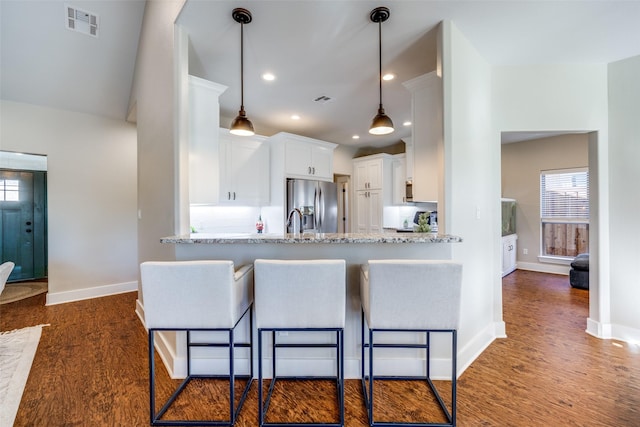 kitchen featuring hanging light fixtures, light stone counters, dark hardwood / wood-style flooring, stainless steel fridge, and white cabinets