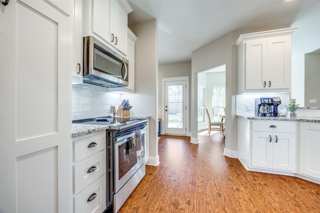 kitchen featuring white cabinets, decorative backsplash, light stone countertops, appliances with stainless steel finishes, and wood-type flooring