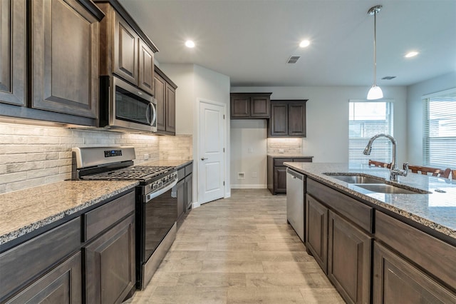 kitchen featuring light stone countertops, stainless steel appliances, sink, decorative light fixtures, and light hardwood / wood-style floors