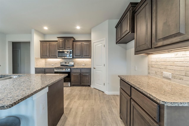 kitchen with sink, stainless steel appliances, backsplash, dark brown cabinets, and light wood-type flooring