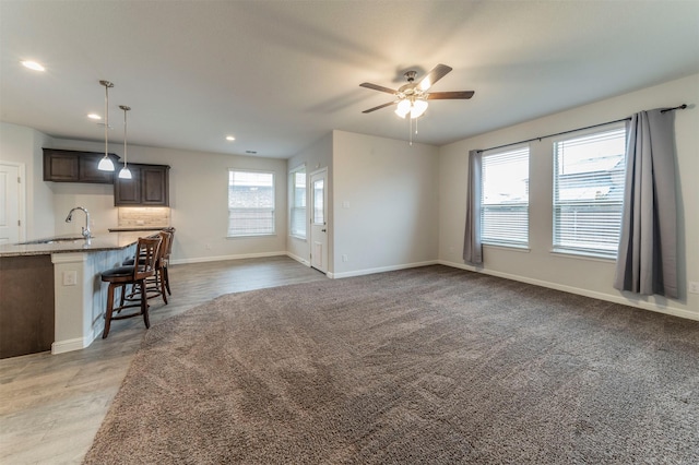 unfurnished living room with ceiling fan, a healthy amount of sunlight, wood-type flooring, and sink