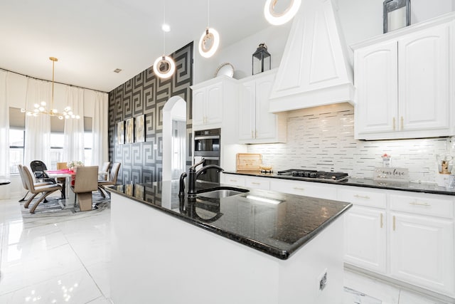 kitchen featuring a center island with sink, white cabinetry, custom range hood, and pendant lighting