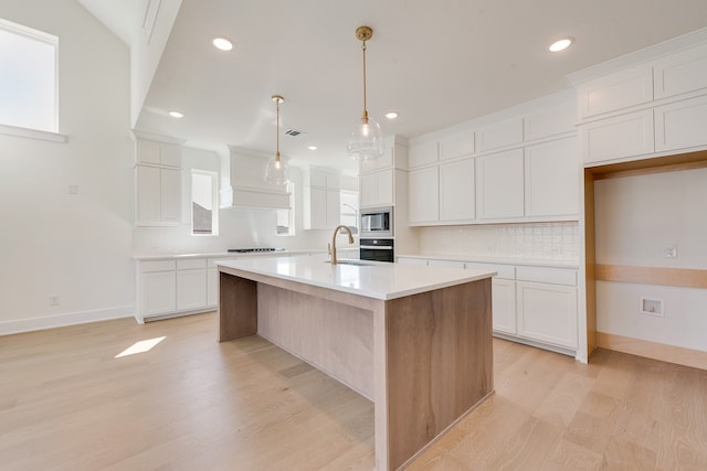 kitchen featuring white cabinetry, sink, stainless steel appliances, light hardwood / wood-style floors, and a center island with sink