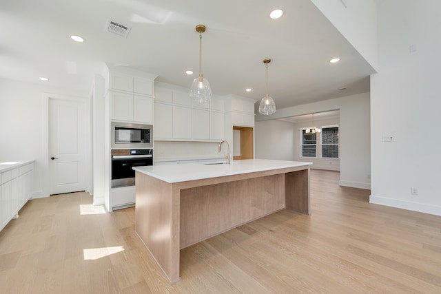 kitchen featuring built in microwave, sink, oven, a center island with sink, and white cabinets