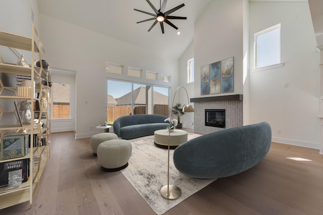 living room featuring a fireplace, wood-type flooring, high vaulted ceiling, and ceiling fan