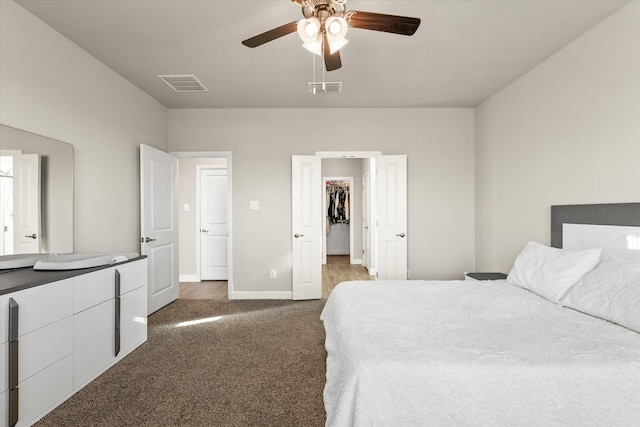 bedroom with dark colored carpet, ceiling fan, a spacious closet, and a closet