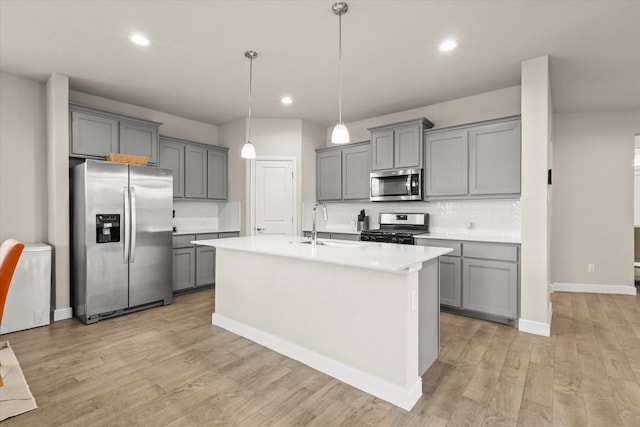 kitchen featuring gray cabinets, stainless steel appliances, hanging light fixtures, and a center island with sink