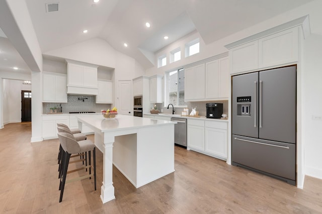 kitchen with high vaulted ceiling, light wood-type flooring, appliances with stainless steel finishes, a kitchen island, and white cabinetry