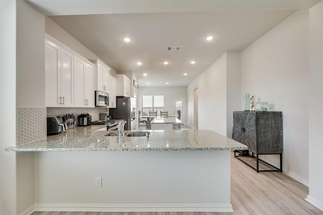 kitchen with light hardwood / wood-style floors, white cabinetry, kitchen peninsula, and appliances with stainless steel finishes