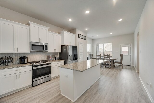 kitchen with a center island, light stone counters, light hardwood / wood-style floors, white cabinets, and appliances with stainless steel finishes