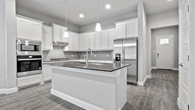 kitchen with appliances with stainless steel finishes, light wood-type flooring, pendant lighting, a center island with sink, and white cabinets