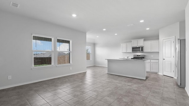 kitchen with a kitchen island with sink, white cabinets, sink, light tile patterned floors, and stainless steel appliances