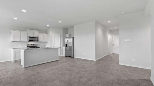 kitchen with light stone counters, stainless steel appliances, sink, a center island with sink, and white cabinets