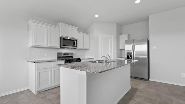 kitchen with white cabinetry, sink, stainless steel appliances, light stone counters, and a center island with sink