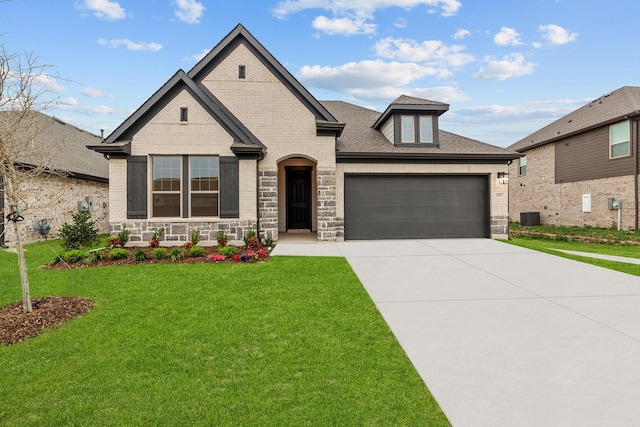french provincial home with a front yard, central AC unit, stone siding, a garage, and concrete driveway