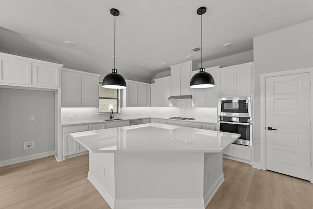 kitchen featuring white cabinets, a sink, light wood-type flooring, appliances with stainless steel finishes, and a kitchen island