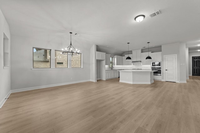 unfurnished living room featuring light wood-style flooring, an inviting chandelier, baseboards, and visible vents