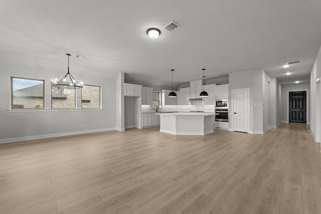 unfurnished living room featuring visible vents, baseboards, light wood-type flooring, and an inviting chandelier