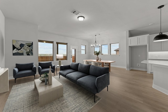 living area with light wood-style flooring, a notable chandelier, visible vents, and plenty of natural light