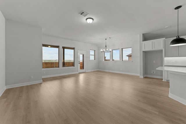 unfurnished living room featuring a chandelier, a wealth of natural light, light wood finished floors, and visible vents