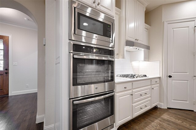 kitchen featuring appliances with stainless steel finishes, backsplash, dark wood-type flooring, crown molding, and white cabinetry